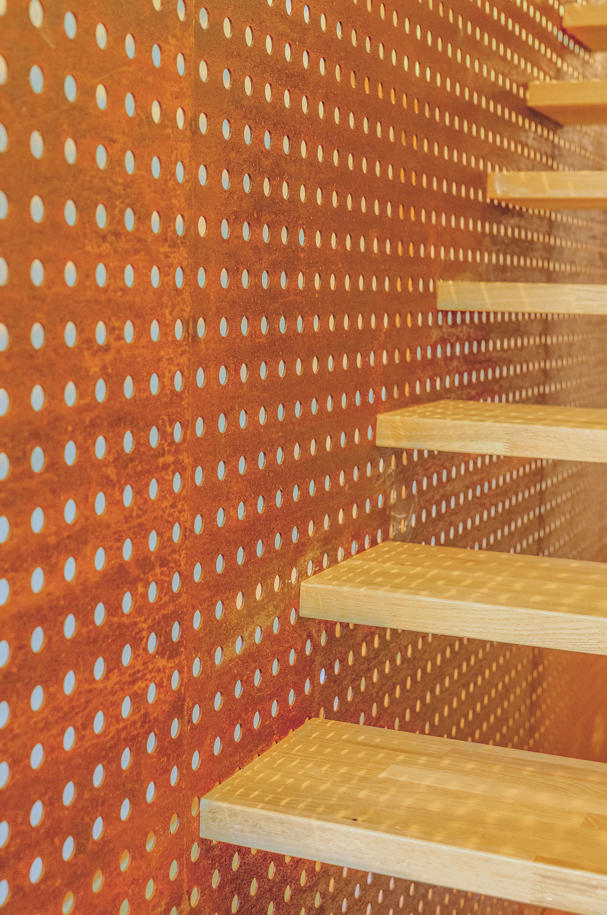 Una serie de escalones de madera con una pared de metal perforado al fondo.