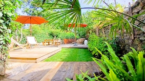 A wooden deck with a grassy area, a dining set, and two large umbrellas. - Maison Brevan (Châteaulin)