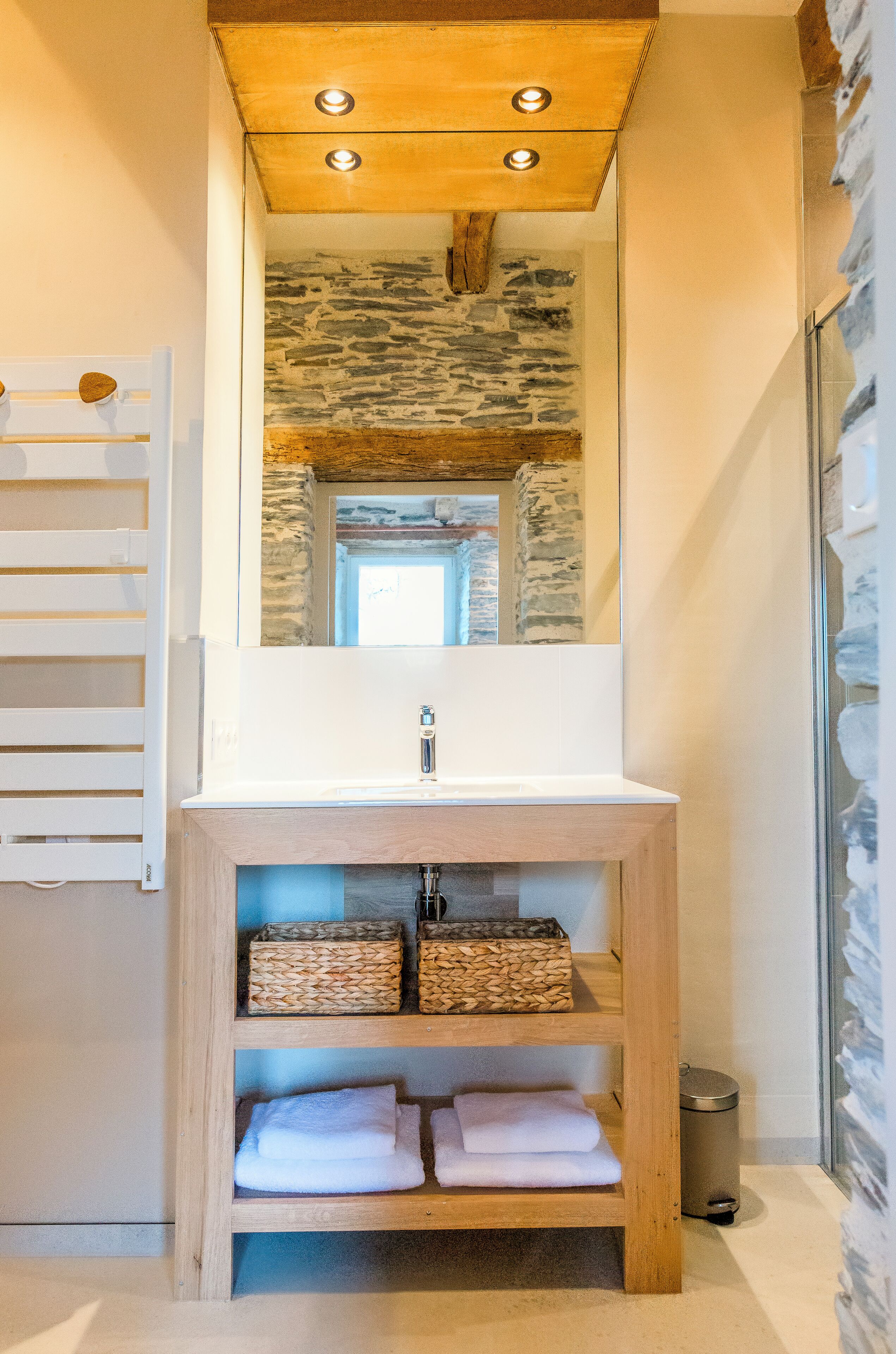 Un baño con tocador de madera, espejo, pared de piedra y cabina de ducha de vidrio.