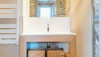Un baño con tocador de madera, espejo, pared de piedra y cabina de ducha de vidrio.