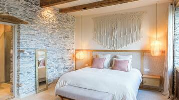 A bedroom with a stone wall, a bed with white bedding, a wooden bench, and two bedside tables with lamps.