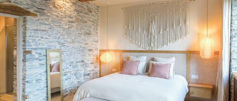 A bedroom with a stone wall, a bed with white bedding, a wooden bench, and two bedside tables with lamps.
