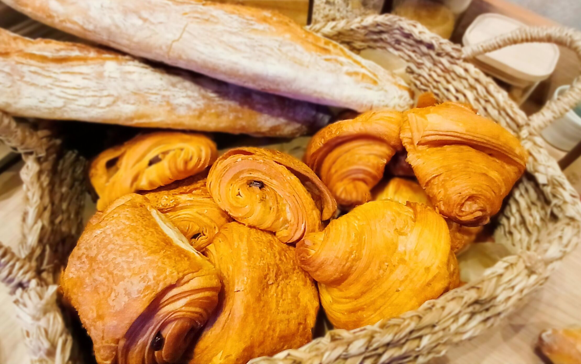 Una cesta con diferentes tipos de pan, incluyendo baguettes y croissants.