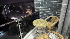 Un balcón con sillas de mimbre, un ventilador y vista a un paisaje urbano nocturno.