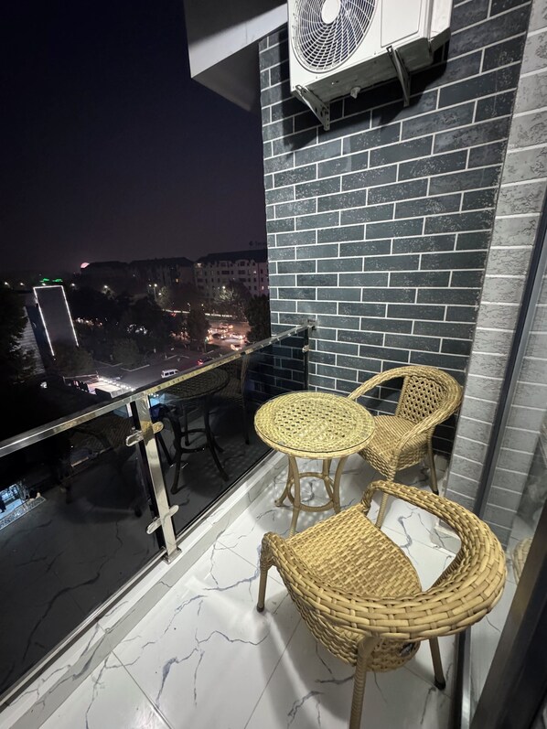 A balcony with wicker chairs, a fan, and a view of a cityscape at night.