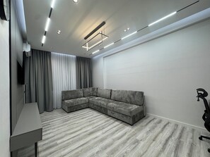 Un salon moderne avec un canapé d’angle, un téléviseur à écran plat et un luminaire suspendu au plafond.