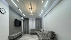 Una sala moderna con un sofá modular, un televisor de pantalla plana, un banco y una lámpara de techo.