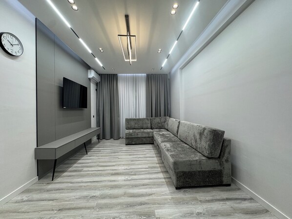 Un salon moderne avec un canapé d’angle, un téléviseur à écran plat, un banc et un luminaire suspendu au plafond.