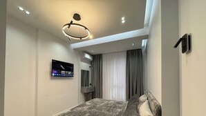 Un dormitorio moderno con una cama, televisor montado y lámpara en el techo.
