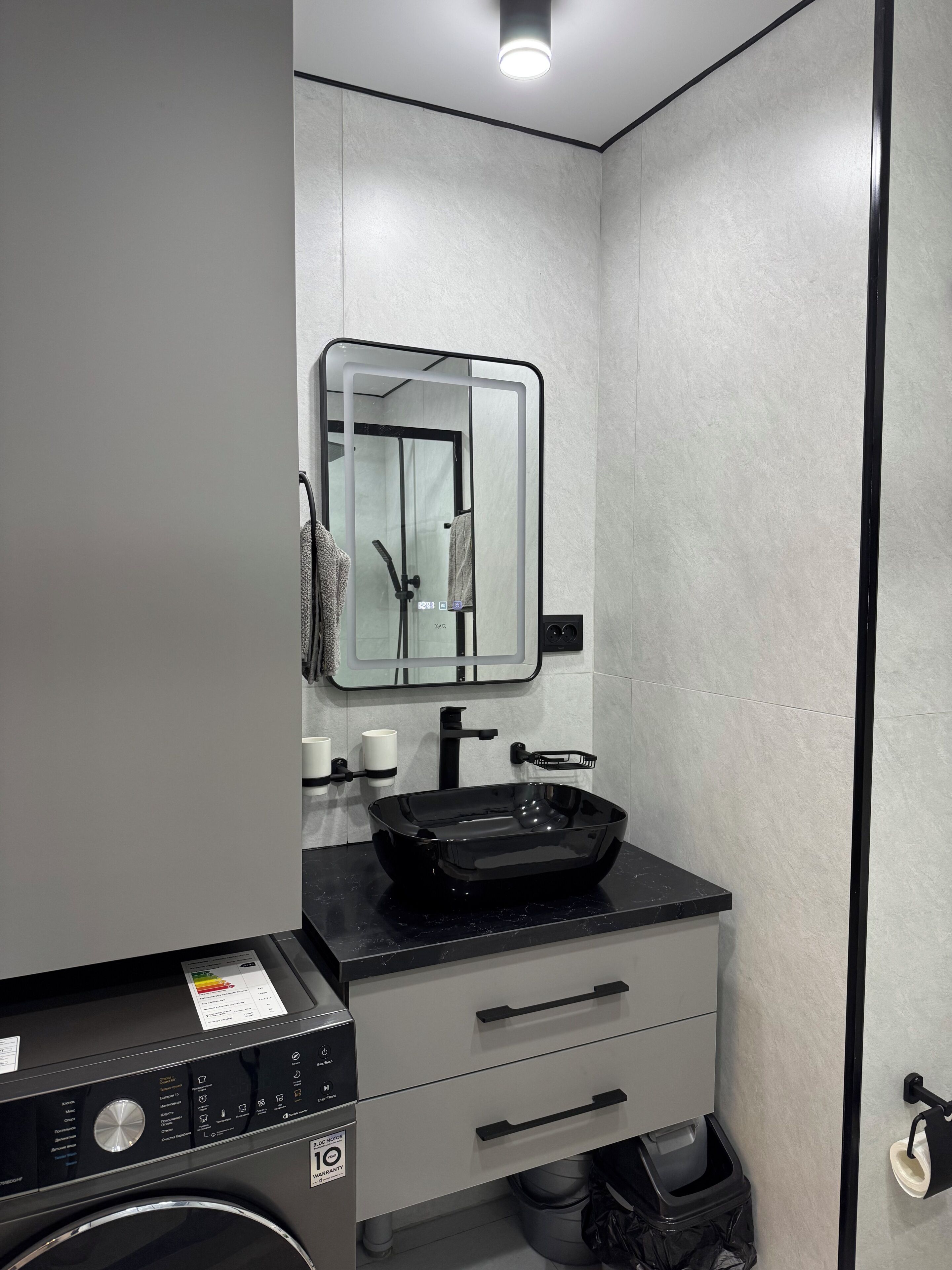 Een moderne badkamer met een zwarte wastafel, een spiegel, een handdoekrek, een toilet en een wasmachine.