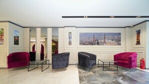 Un hall d’entrée avec des canapés rouges, une table basse en verre et un grand tableau représentant un paysage urbain accroché au mur.