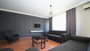 Un salon moderne avec un téléviseur à écran plat fixé au mur, une table basse en verre et deux canapés gris.