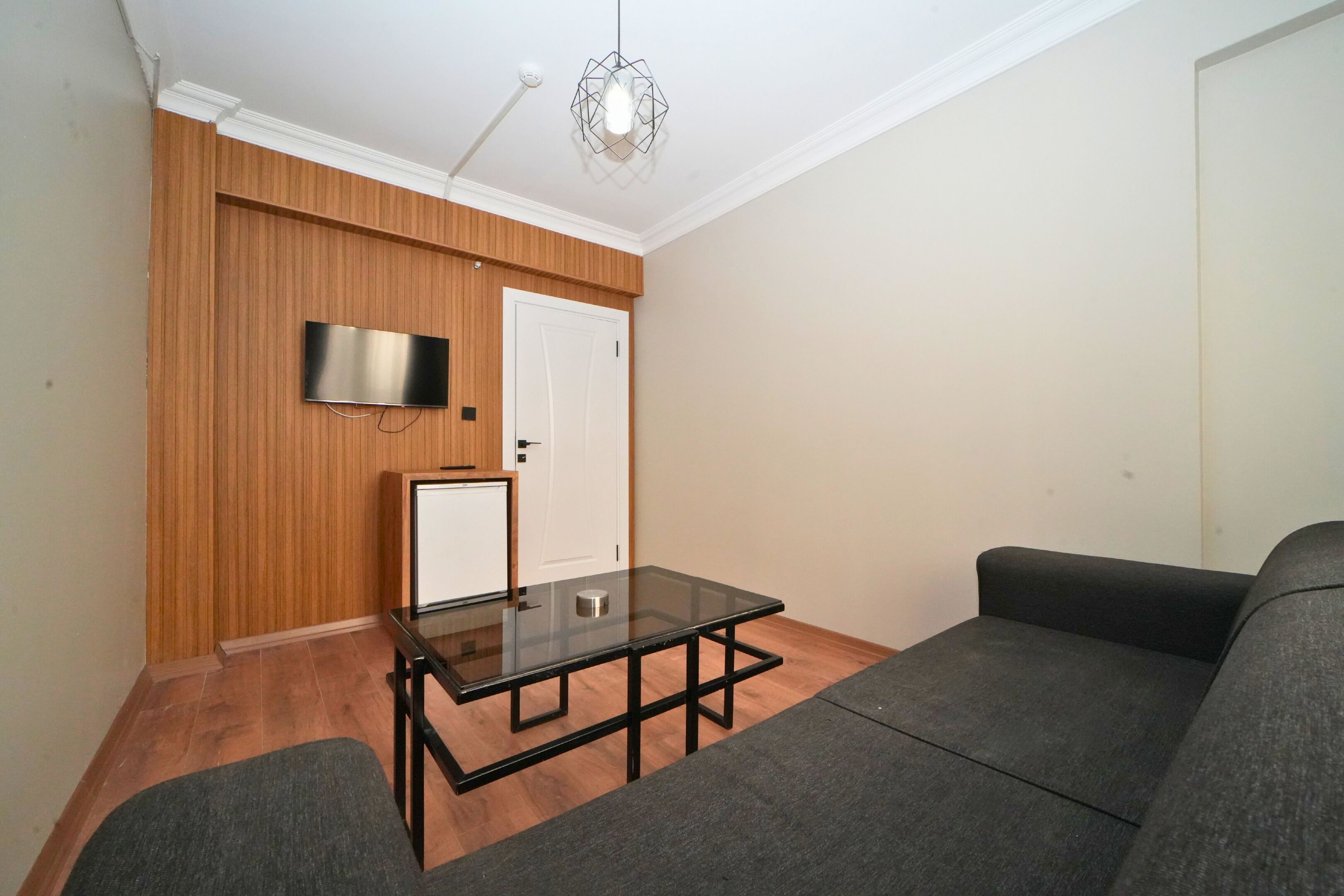 Un salon comprenant un canapé, une table basse avec un plateau en verre, un téléviseur à écran plat fixé à un mur en bois et une porte.