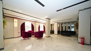 Un hall d’entrée spacieux, doté d’un sol carrelé brillant, de chaises rouges et d’un extincteur.