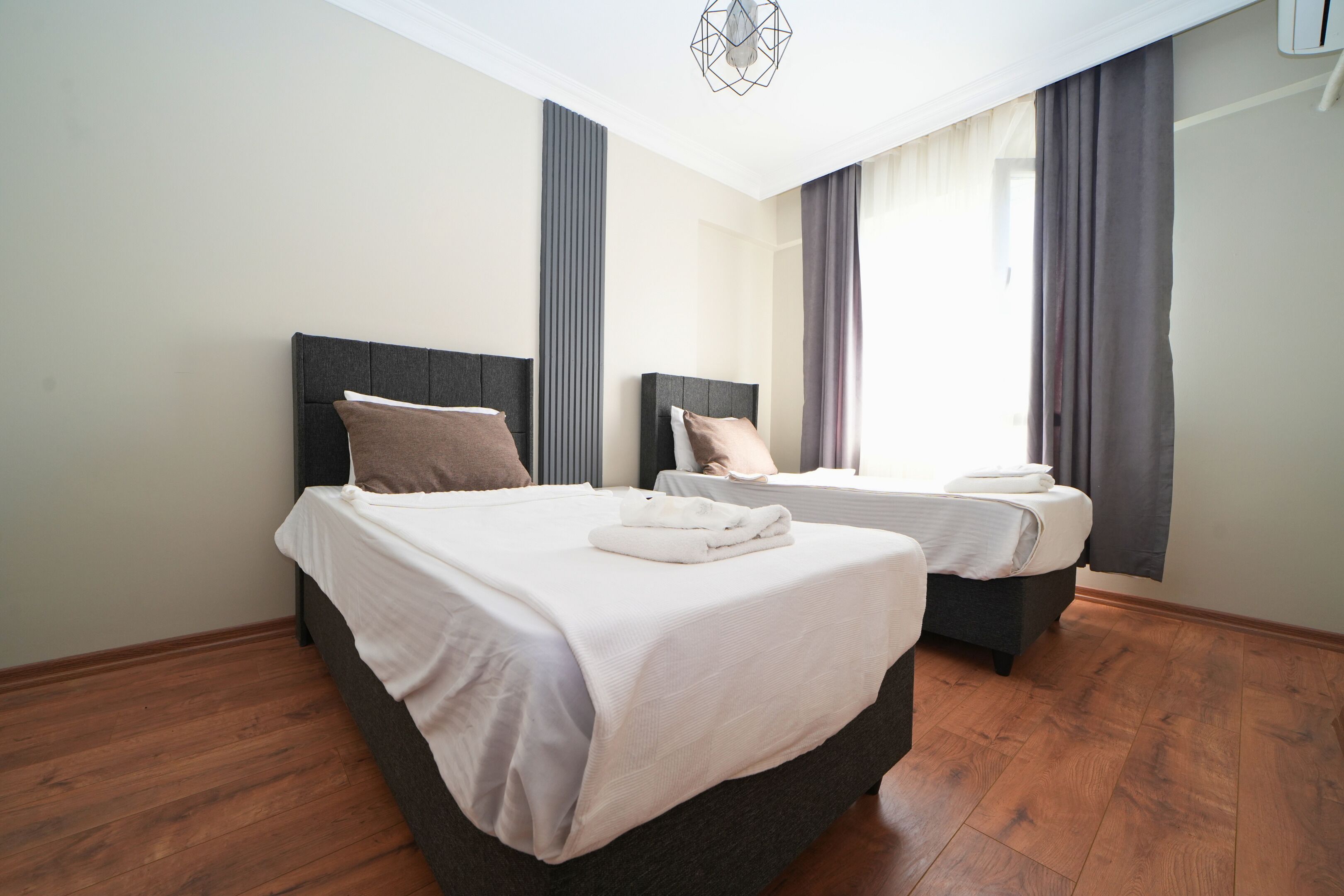 Habitación de hotel con dos camas, piso de madera y una lámpara de techo moderna.