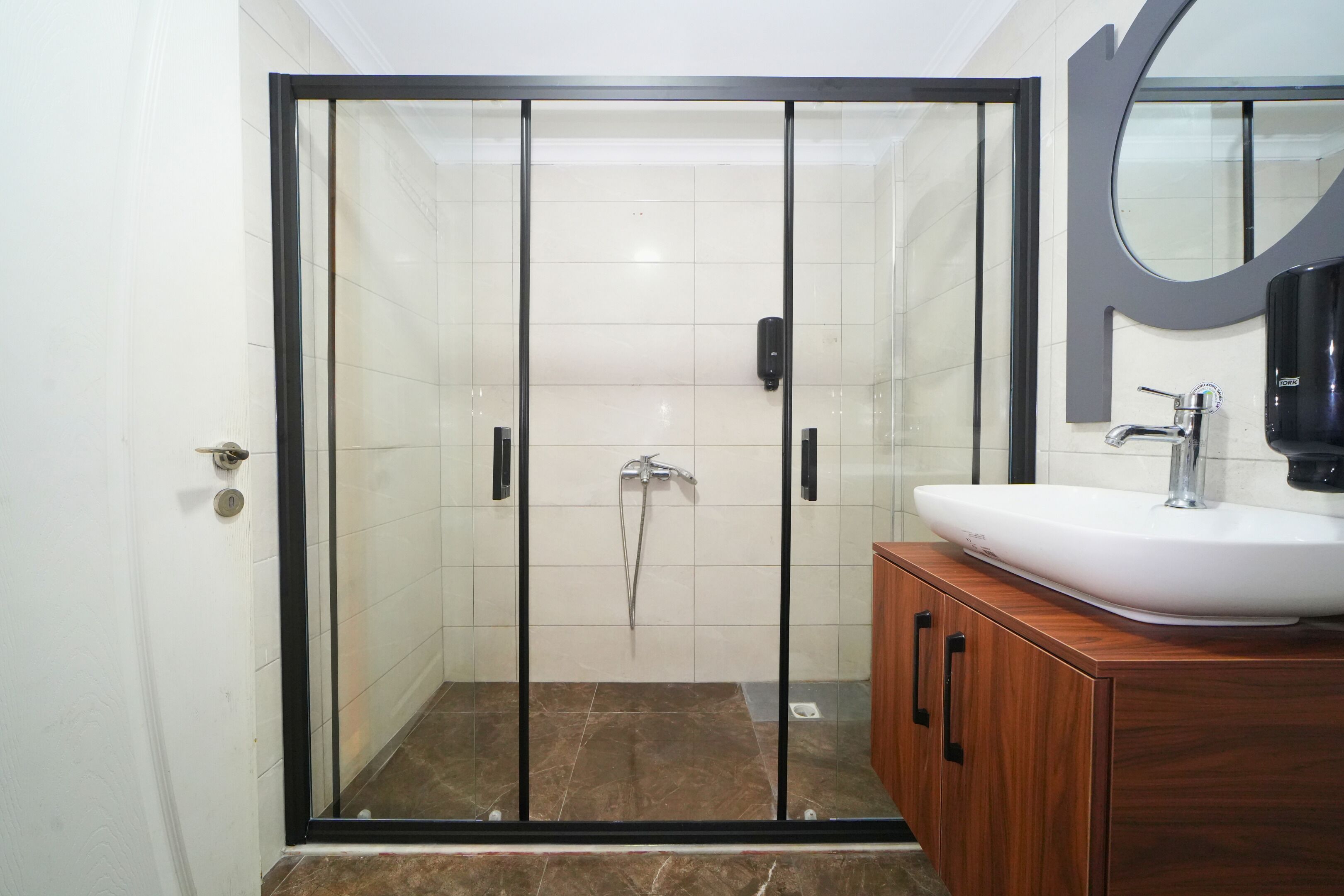 Un baño moderno con ducha envuelta en vidrio, un lavamanos blanco y muebles de madera.