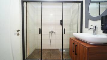 Un baño moderno con ducha envuelta en vidrio, un lavamanos blanco y muebles de madera.
