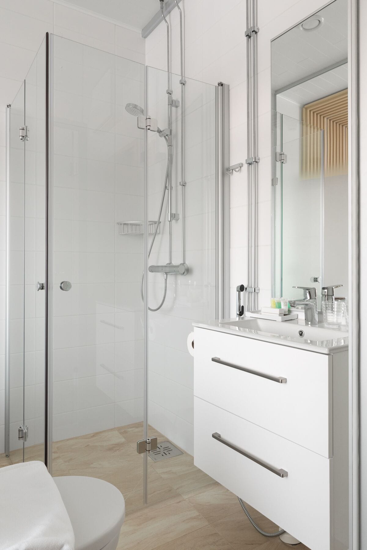 Un baño moderno con ducha envuelta en cristal, un tocador blanco con espejo y un inodoro.