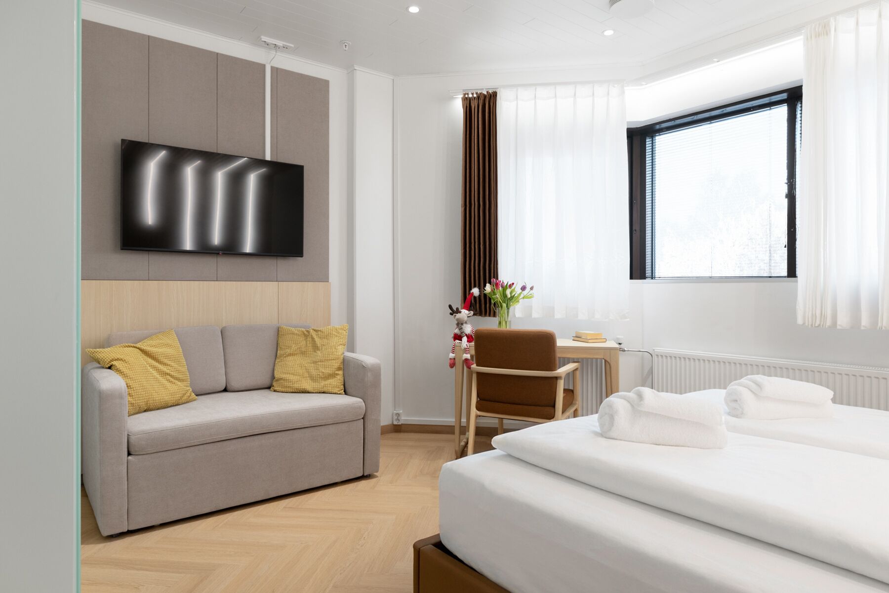 A modern hotel room with a sofa, a bed, a TV, a chair, and a window.