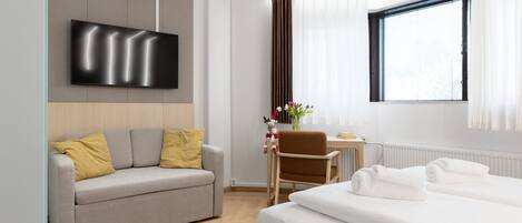 A modern hotel room with a sofa, a bed, a TV, a chair, and a window.
