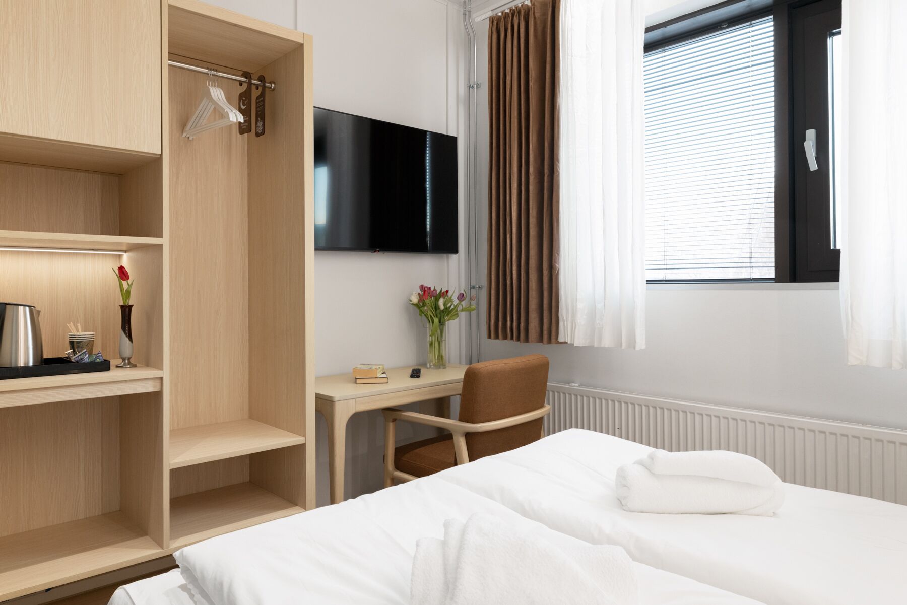 Une chambre d’hôtel équipée d’un lit, d’un bureau, d’une chaise, d’une télévision et d’une fenêtre avec des rideaux.