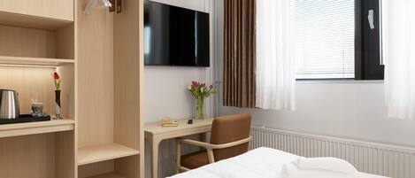 A hotel room with a bed, a desk, a chair, a TV, and a window with curtains.