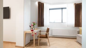 A modern room with a wooden floor, a desk with a chair, a radiator, and a window with curtains.