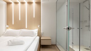 A modern hotel room with a bed, bedside table, and a glass-enclosed shower area. - Polar Nook Hotel (Rovaniemi)