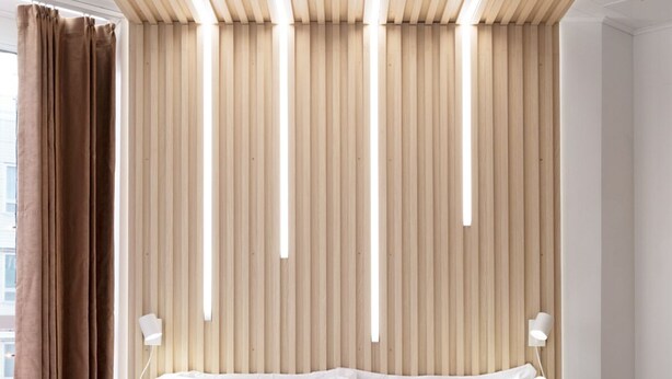 A modern hotel room with a large bed, wooden slats on the ceiling, and a view of the city. - Polar Nook Hotel (Rovaniemi)