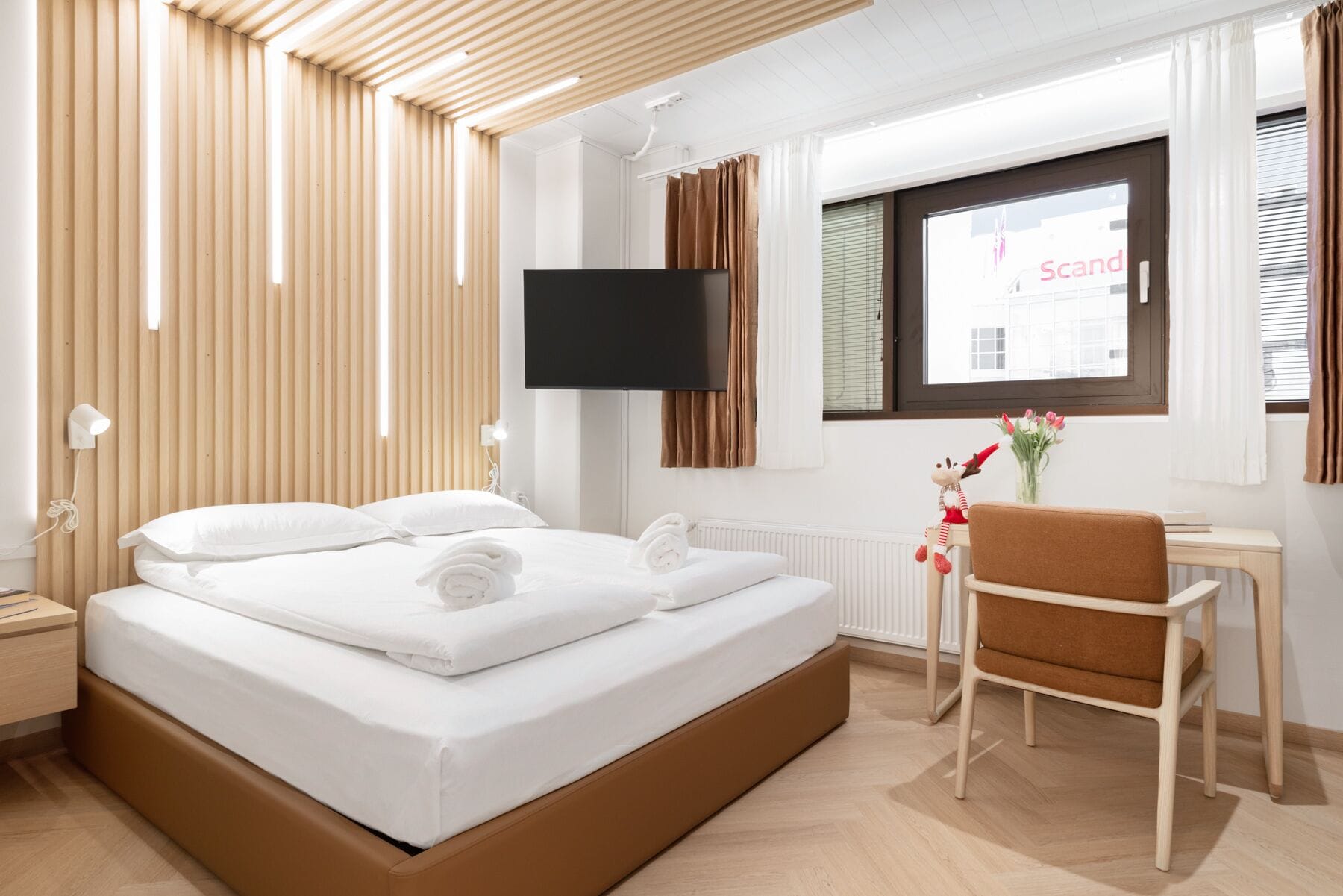A modern hotel room with a large bed, a desk, a chair, a TV, and a window with curtains.