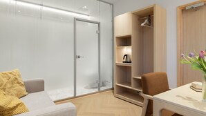 A modern room with a glass door, a wooden wardrobe, a grey sofa, a brown chair, and a small table with a vase of flowers. - Polar Nook Hotel (Rovaniemi)