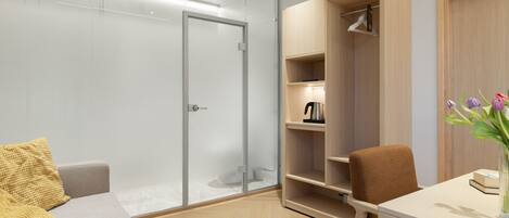 A modern room with a glass door, a wooden wardrobe, a grey sofa, a brown chair, and a small table with a vase of flowers.