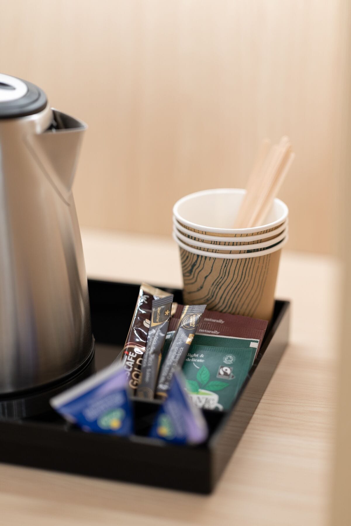 A tray with a coffee maker, a stack of cups, and some packaged food items.