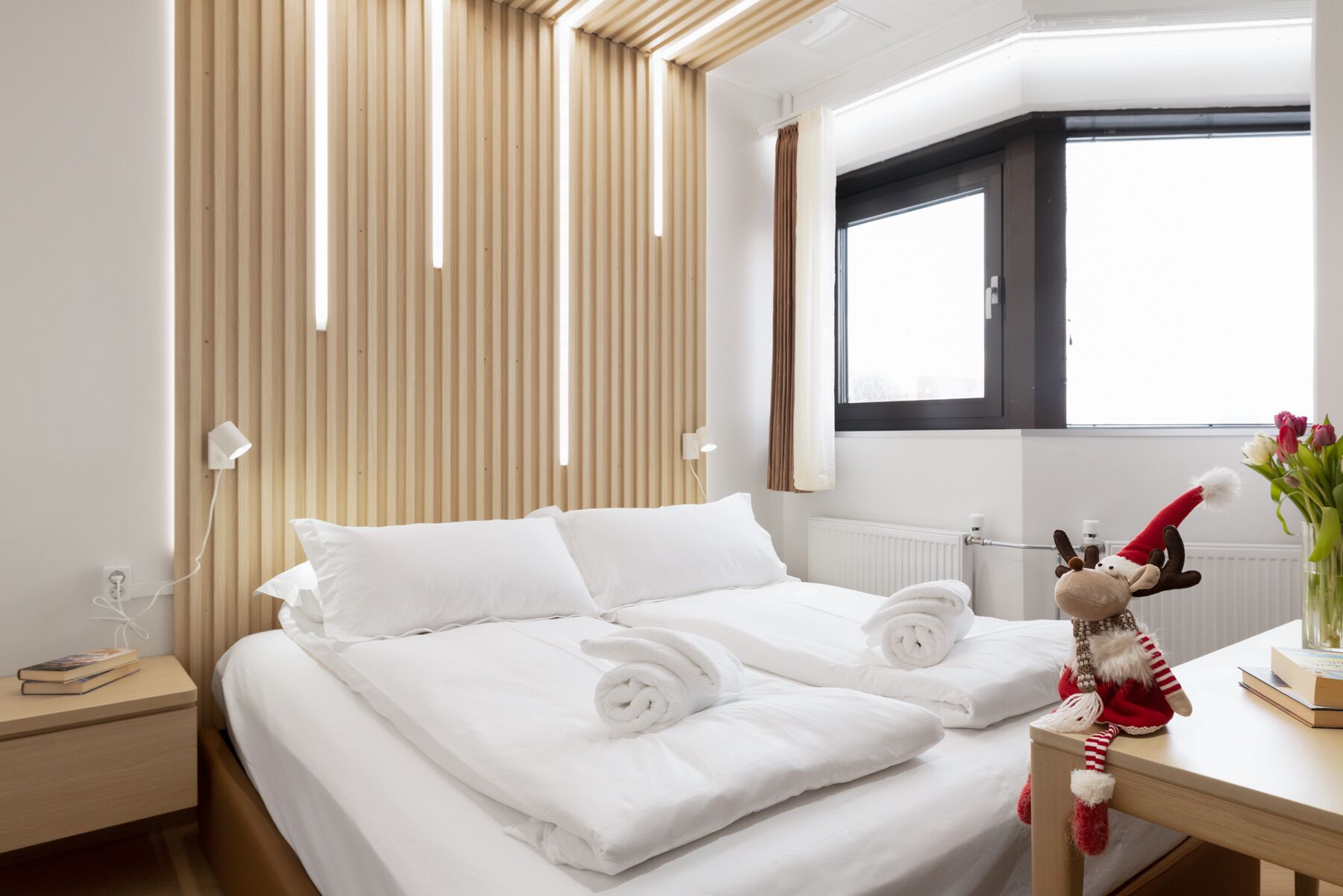 Une chambre d’hôtel avec un lit, une table de chevet, une fenêtre et un jouet en peluche posé sur la table.