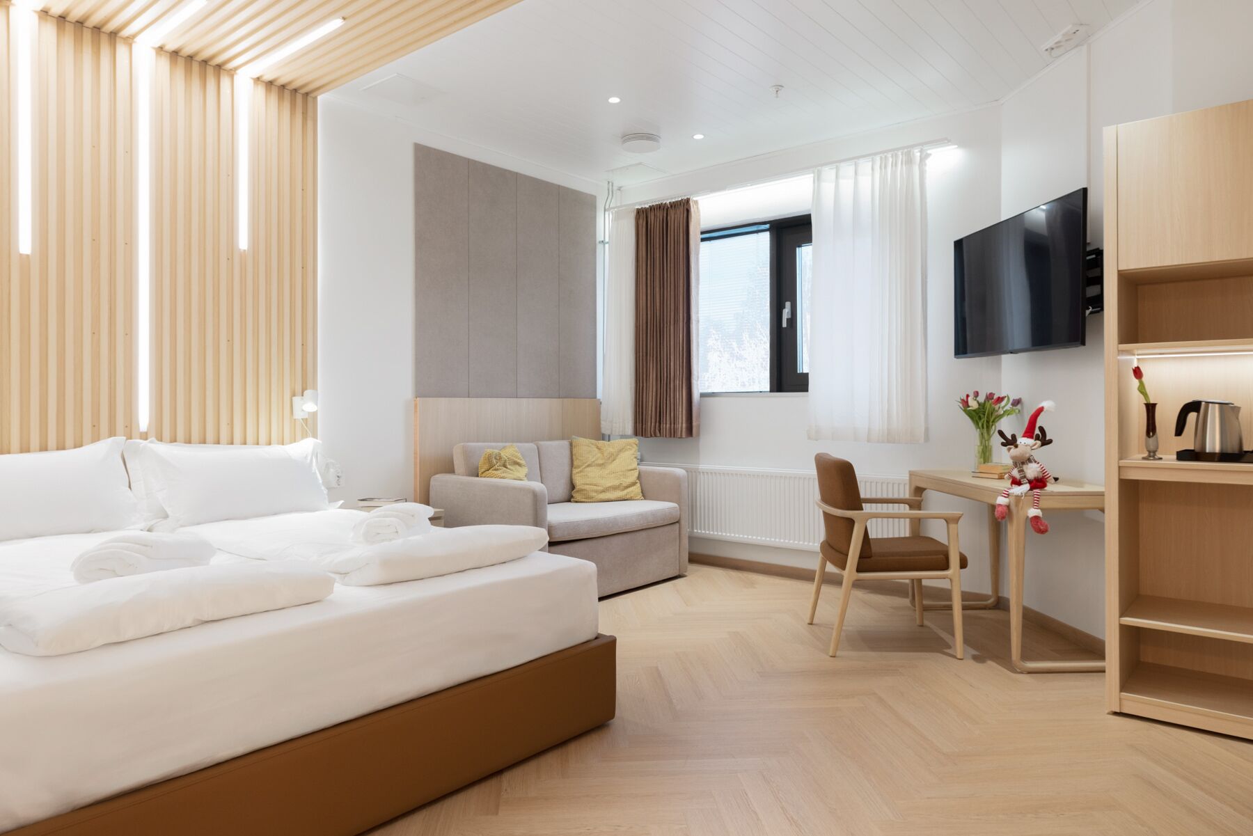 A modern hotel room with a bed, a sofa, a desk, and a TV.