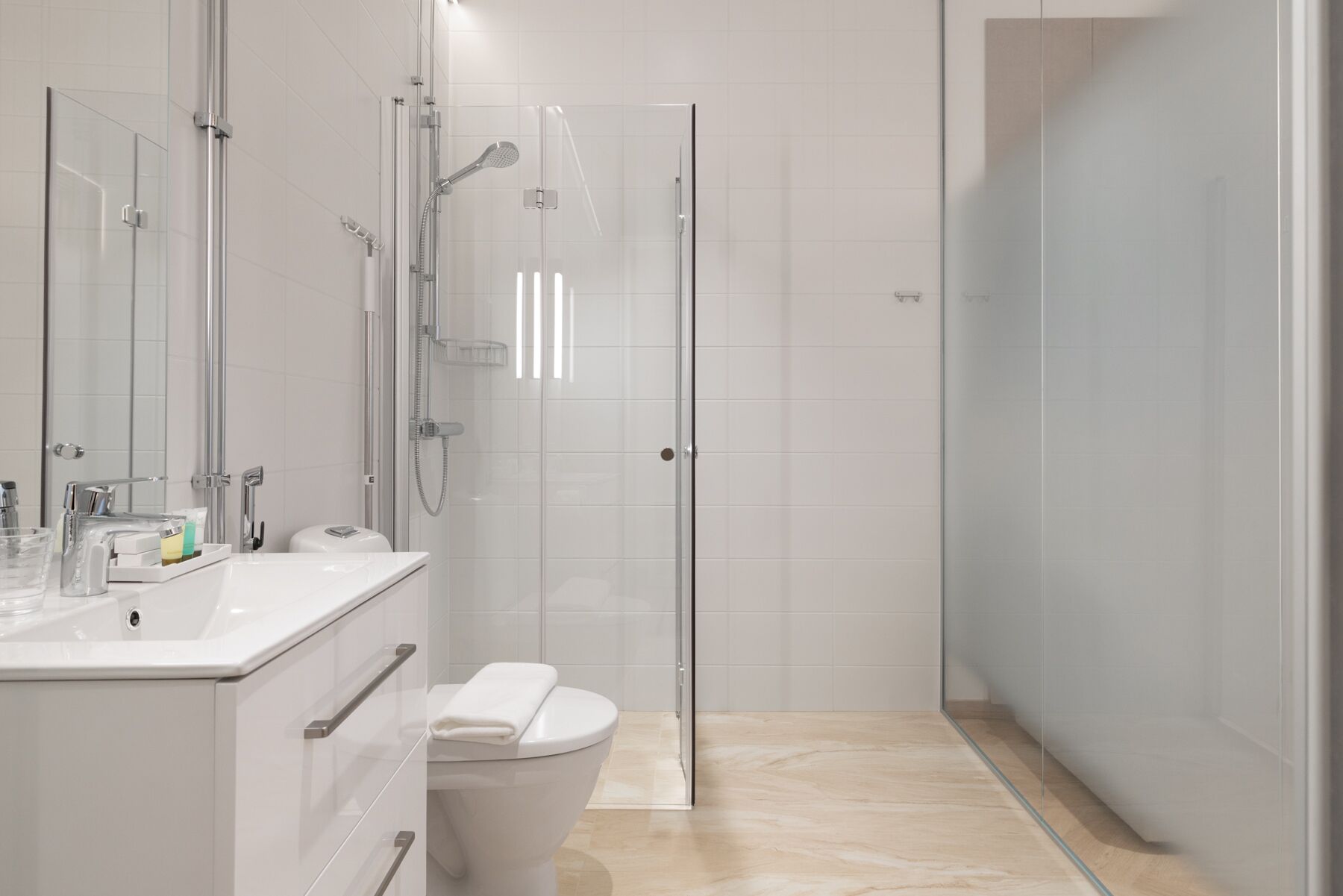 Un baño moderno con ducha envuelta en vidrio, un inodoro blanco y un lavamanos con espejo y lavabo.
