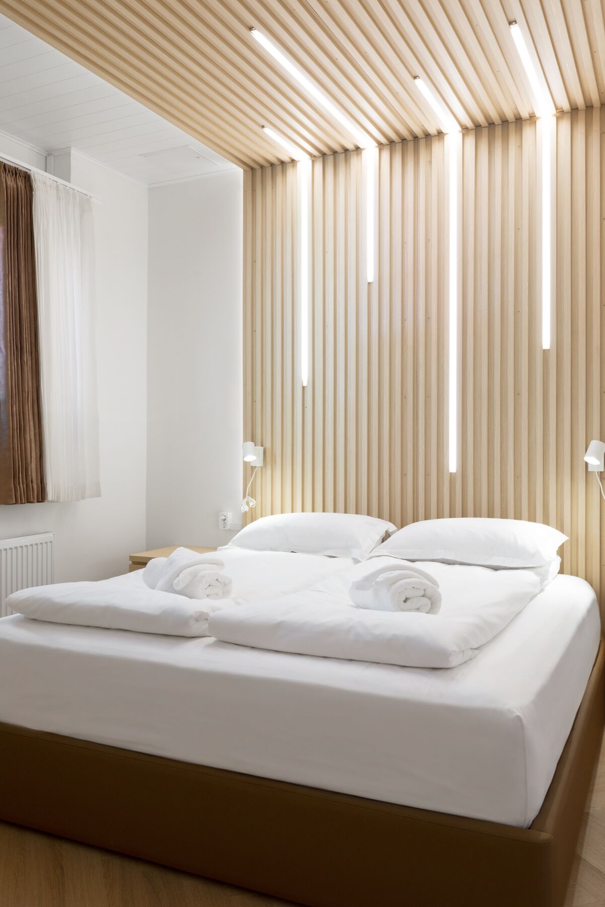 Een moderne hotelkamer met een houten lambrisering, een net opgemaakt bed met witte lakens en een wandlamp.