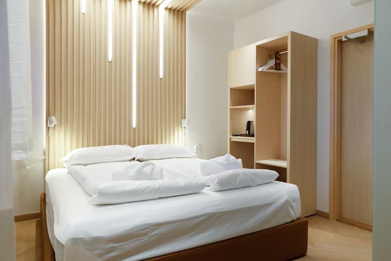 A modern bedroom with a wooden bed, built-in wardrobe, and a vertical light panel.