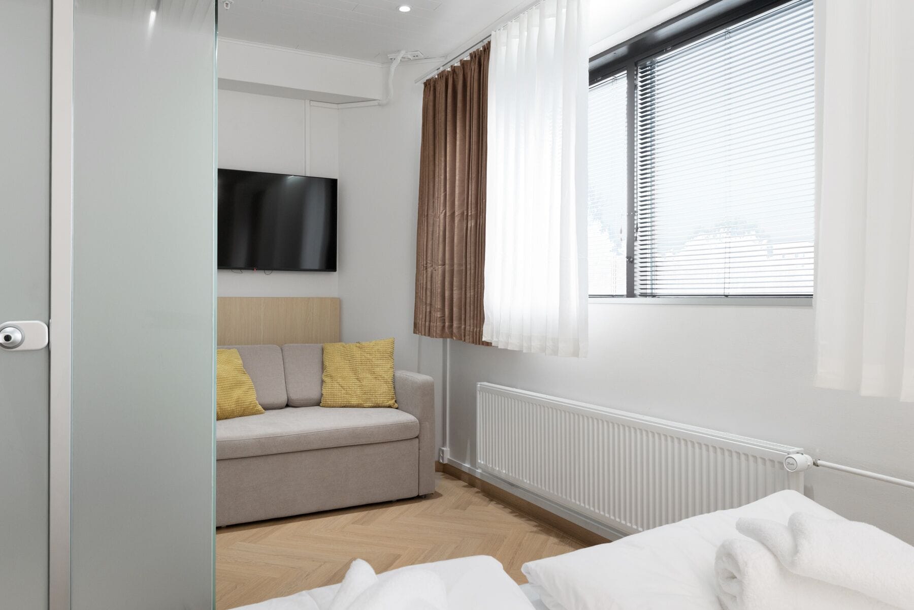 A modern room with a sofa, a TV, a window with blinds, and a radiator.