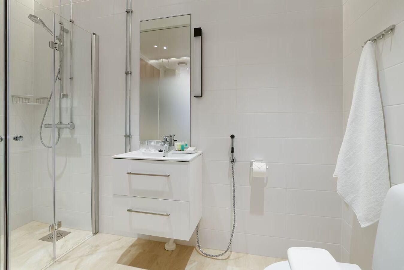 A modern bathroom with a glass shower enclosure, a white sink with a mirror, and a towel rack.