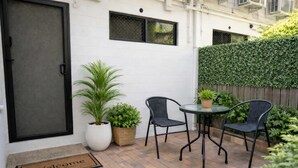 Un patio con una mesa, dos sillas, una planta en maceta y un felpudo.