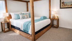 Una cama con dosel de madera, ropa de cama blanca y detalles azules. Hay dos mesitas de noche con lámparas y velas.