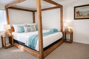 Un lit à baldaquin avec une structure en bois, une literie blanche et des touches de couleur bleue. Il y a deux tables de chevet avec des lampes et des bougies.