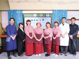 A group of people standing in a room with a banner displaying Japanese characters.