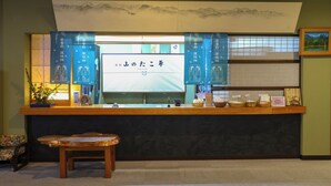 A reception desk with a wooden counter, a bench, and a wall-mounted screen displaying text. - Yamano Takohei (Azumino)