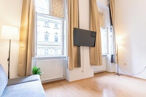 A modern living room with a large window, a flat-screen TV mounted on the wall, and a floor lamp. - Private Room Long Stay Near Lugner City (Vienna)