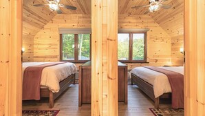 Une cabane avec deux lits en bois, un bureau et une fenêtre donnant sur la forêt.