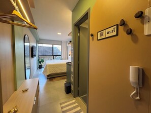 Une chambre d’hôtel avec un lit, une table de chevet et un petit bureau. Une porte donne accès à une autre pièce et la fenêtre offre une vue sur l’extérieur.