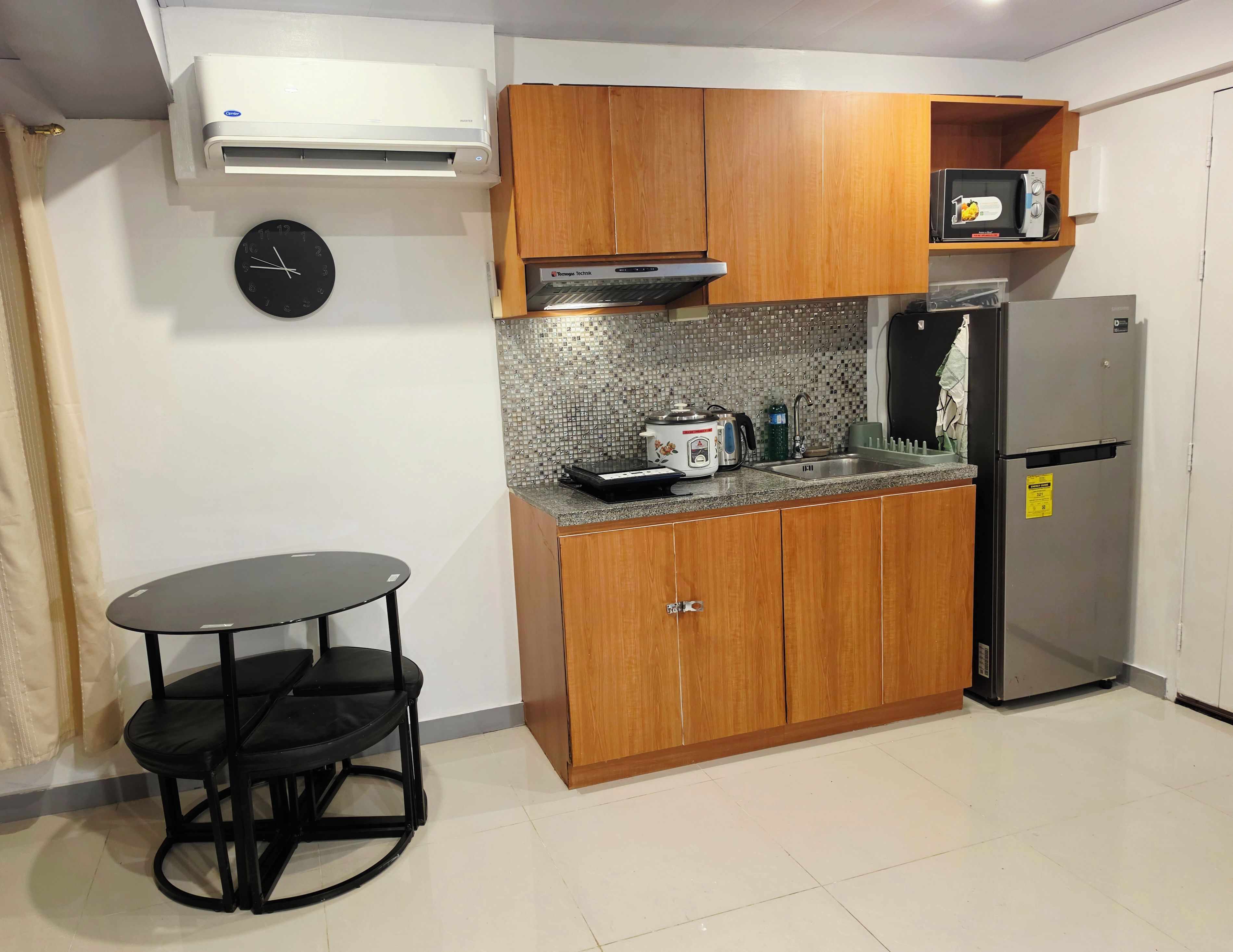 A compact kitchen with wooden cabinets, a microwave, a refrigerator, and a small dining table with chairs.