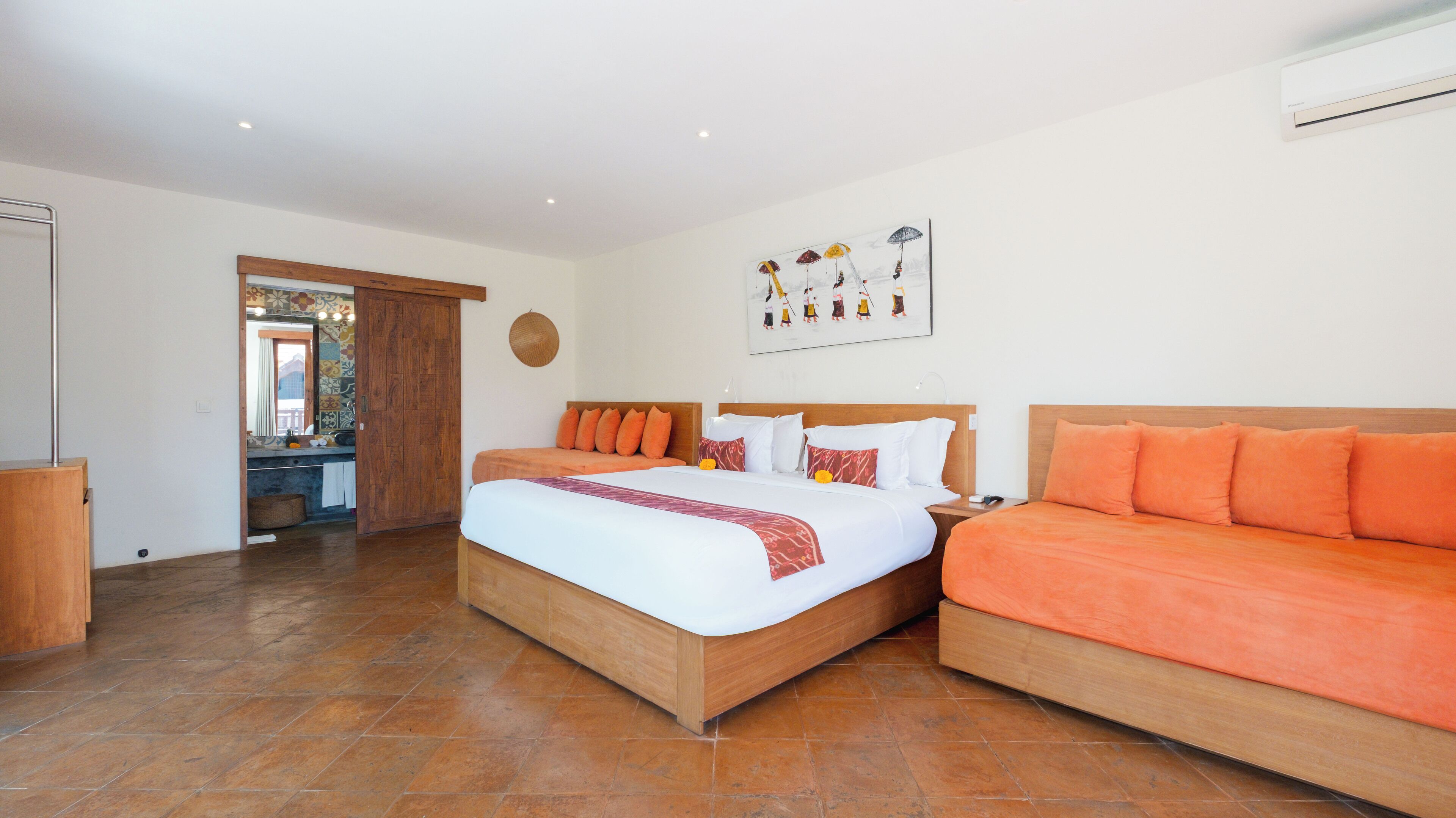 A hotel room with a large bed, a sofa, a wooden floor, and a bathroom visible through an open door.